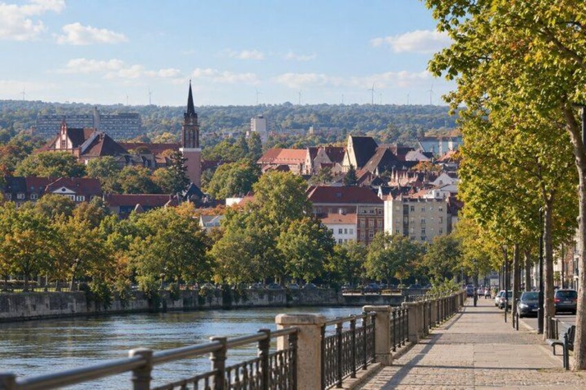 A riverside walkway with a bridge, buildings, and a church spire in the background. 5