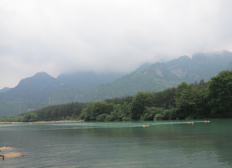 A calm river with boats, surrounded by dense green forest and mist-covered mountains. 2