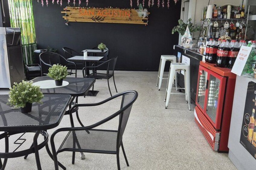 A cafe interior with tables, chairs, a counter with drinks, and a sign on the wall. 5