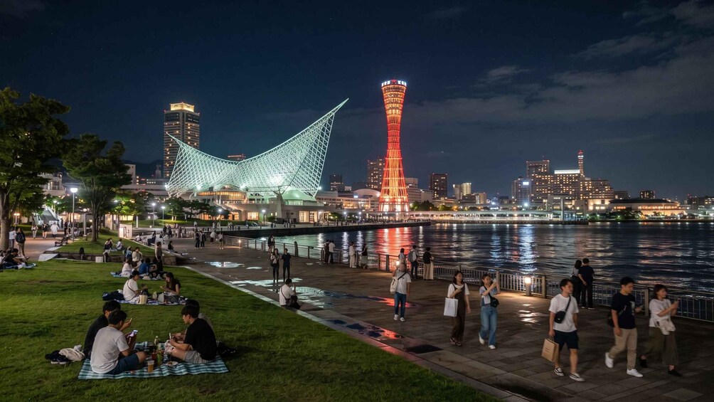 A riverside walkway with people walking and sitting, illuminated buildings, and a bridge. 2