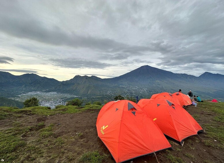 Un paysage montagneux où l’on aperçoit plusieurs tentes orange installées sur une pente herbeuse. 2
