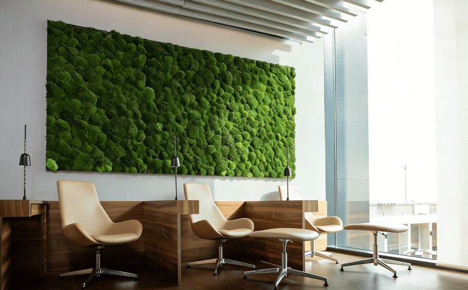 A modern interior with a green moss wall, wooden reception desk, and two beige chairs. 2