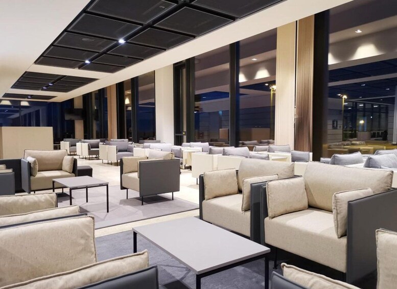 A modern indoor seating area with sofas and tables, large windows, and a ceiling with recessed lighting. 1