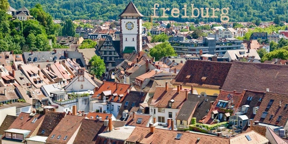 Une ville qui se distingue par son imposant beffroi, ses bâtiments traditionnels et une colline verdoyante qui se dresse à l’arrière-plan. 3
