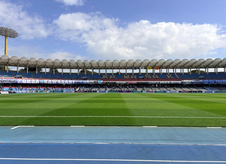 A stadium with blue seats, a green field, and a clear sky. 1
