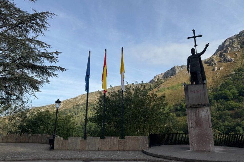 A statue with a cross, flags, and a mountainous background. 3