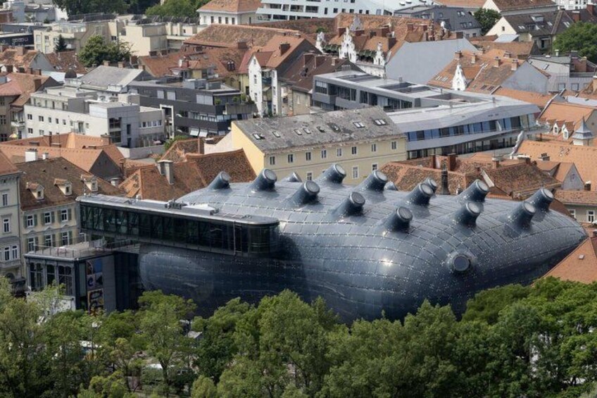 A modern building with a unique, rounded roof structure surrounded by traditional buildings. 4