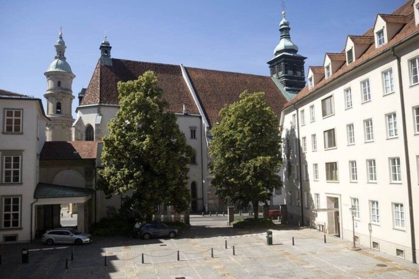 A historic European town square with buildings, trees, and a church. 2