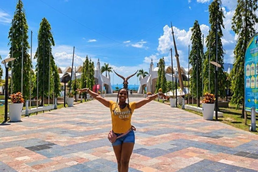 A person in a yellow shirt and blue shorts standing on a patterned pavement with trees and buildings in the background. 4