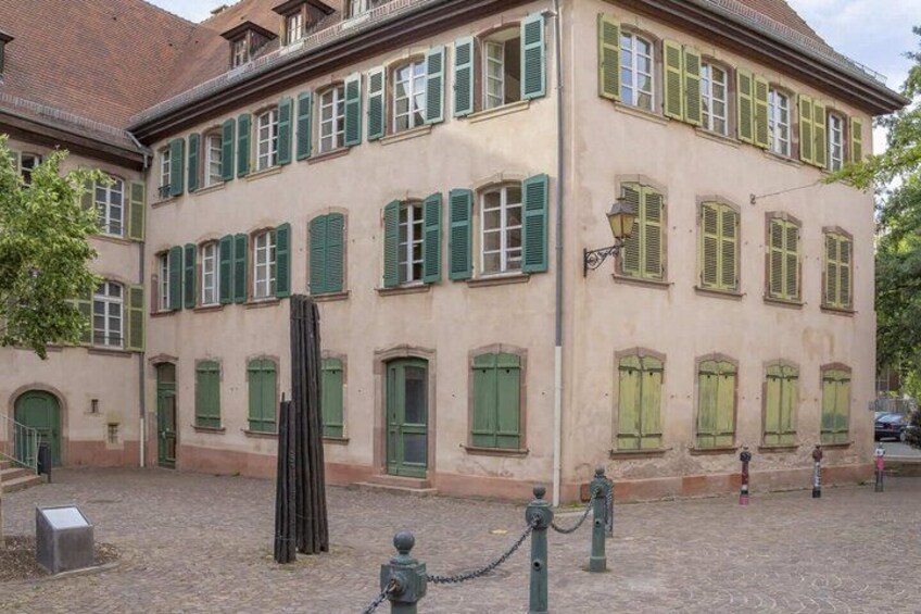 A historic building with green shutters, a cobblestone courtyard, and a statue. 3