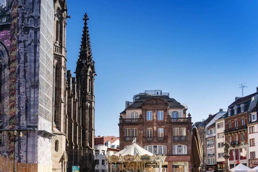 A historic cathedral with Gothic architecture, a traditional market square with a carousel, and classic European buildings. 1