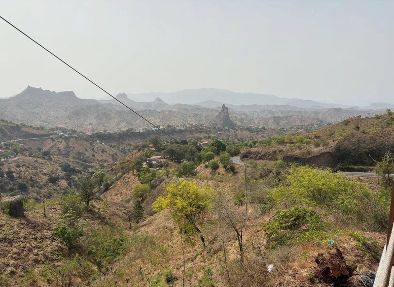 A mountainous landscape with a prominent peak, scattered vegetation, and a winding road. 5