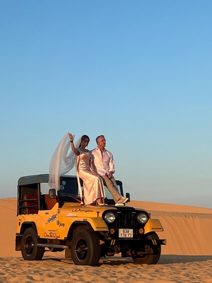 Un couple, vêtu de leurs habits de mariage, se trouve à bord d’un véhicule de safari dans un désert. 3
