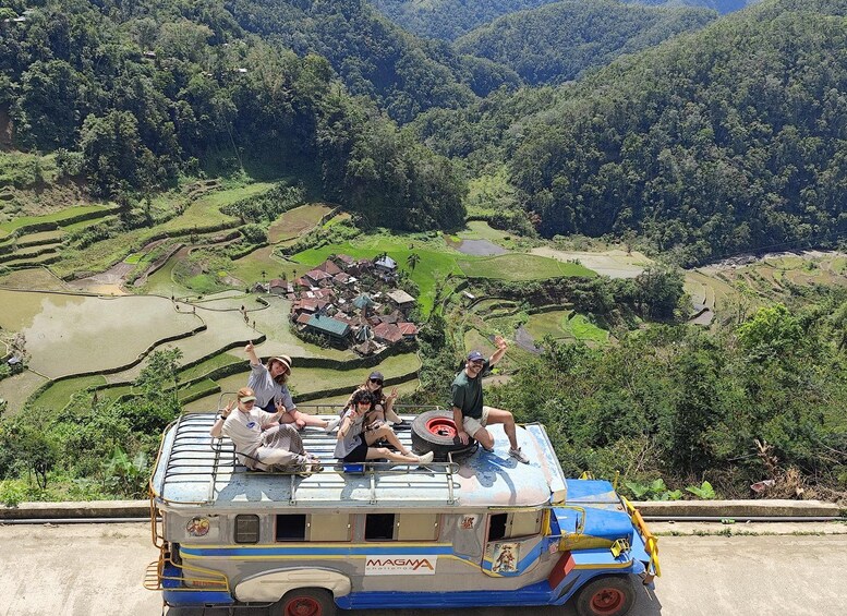 A group of people on a colorful bus with a scenic view of terraced fields and a village in the background. 4