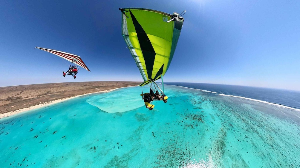 A paraglider flying over a turquoise sea with a clear sky. 1