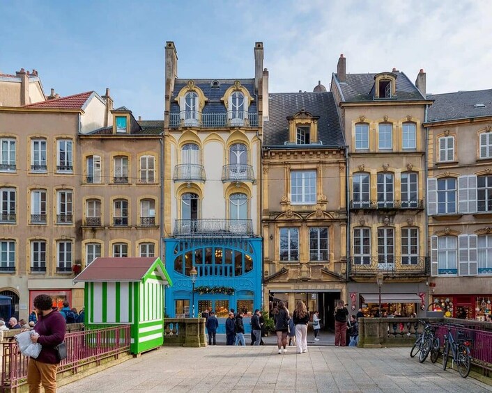 A historic European square with ornate buildings, a blue kiosk, and people walking. 2