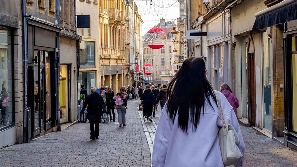 A cobblestone street lined with historic buildings, pedestrians walking, and a red spherical object hanging above. 4