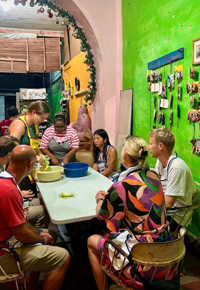 Eine Gruppe von Menschen sitzt an einem Tisch in einem Raum mit grüner Wand und ist beim Kochen beschäftigt. 5