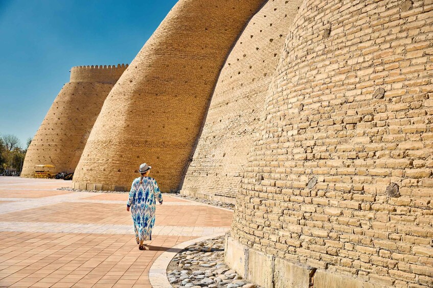 A person walking past ancient brick structures with a clear blue sky. 2