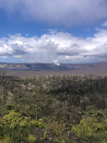 A landscape with a volcano emitting smoke, a forested area in the foreground, and a cloudy sky. 3