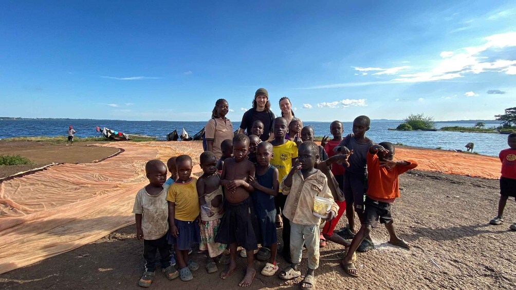 A group of people, including children, standing on a sandy beach with a body of water in the background. 3