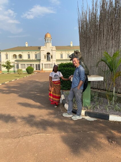 A building with a dome and arched windows, a person in a striped skirt, and another person leaning on a fence. 1