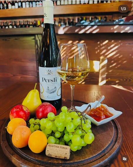 A bottle of wine, a glass of wine, and a variety of fruits on a wooden table. 2