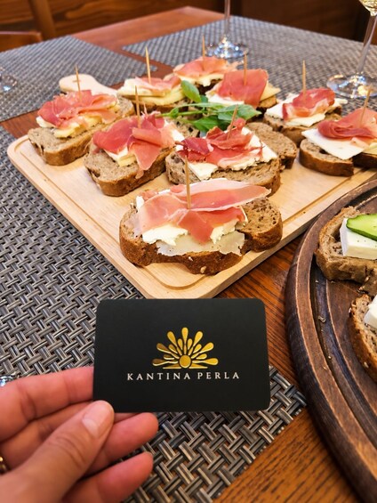 A wooden board with various sandwiches, a wine glass, and a logo card. 3