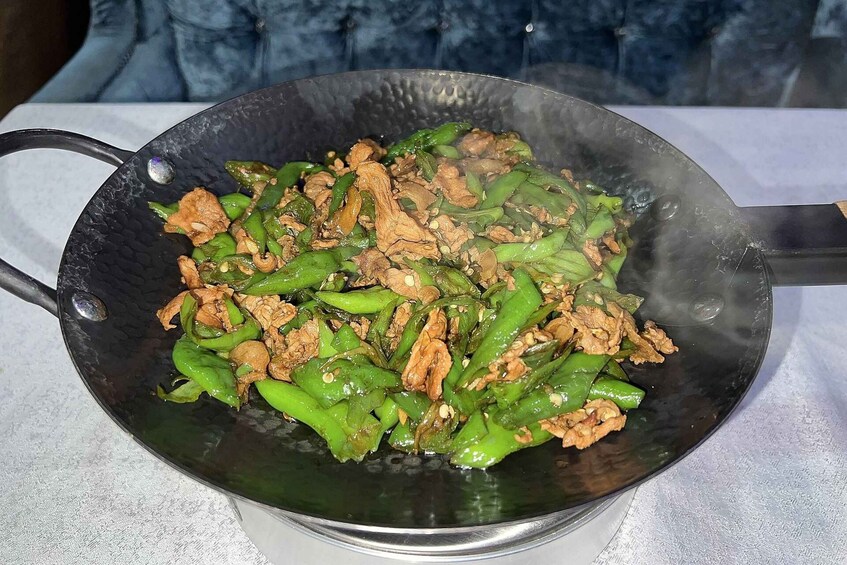 A wok with stir-fried vegetables and meat, possibly chicken, on a stove. 3