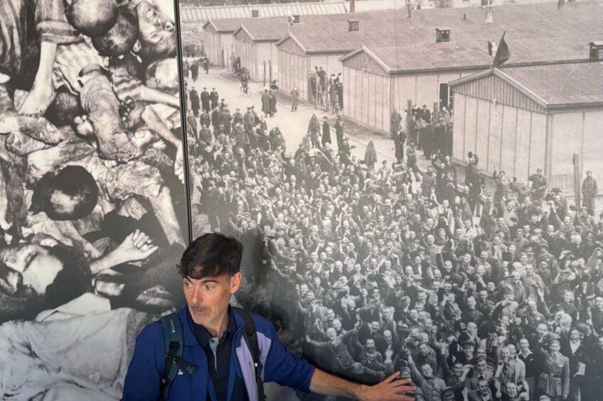 A man standing in front of a large historical photograph depicting a crowded scene with buildings and people. 4