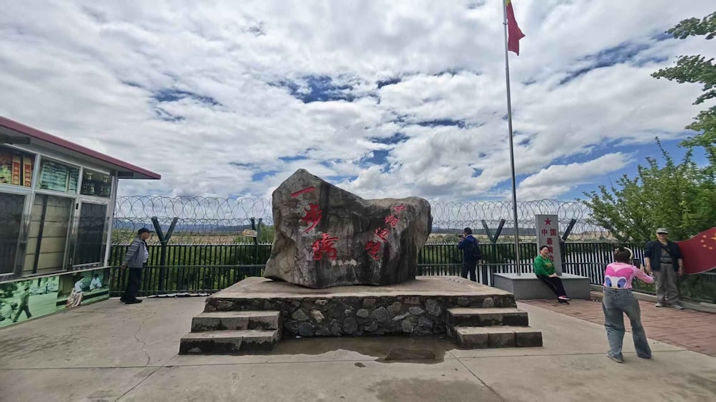 A large rock with red inscriptions, a flagpole with a flag, and a building with barred windows. 2