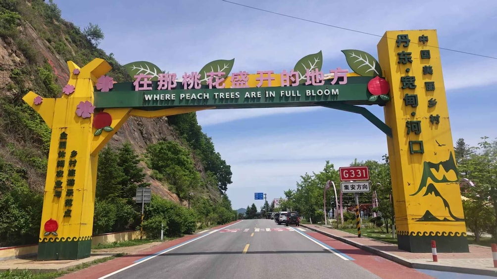 A road with a large archway featuring peach trees and a sign that reads 'Where peach trees are in full bloom.' 4
