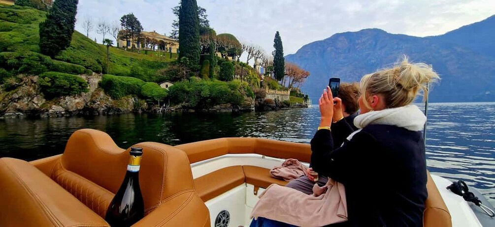 A boat on a lake with a person taking a photo, a bottle, and a scenic landscape with houses and mountains in the background. 5