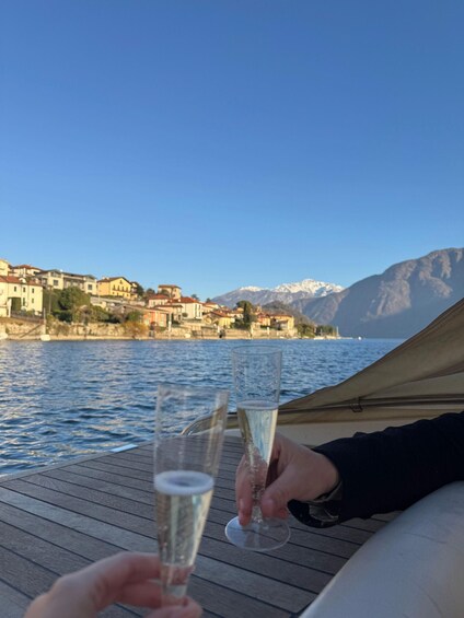Two people holding champagne glasses on a boat, with a lake and mountains in the background. 2