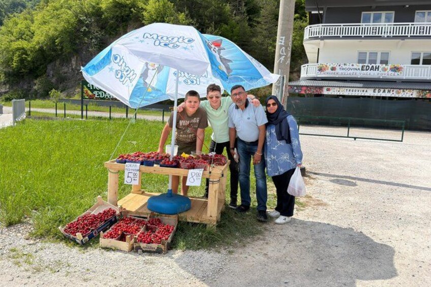 A fruit stand with strawberries and cherries, a blue umbrella, and a building in the background. 4