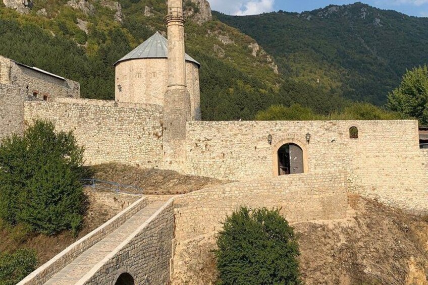 A historic stone fortress with a watchtower, a bridge, and a mountainous backdrop. 3
