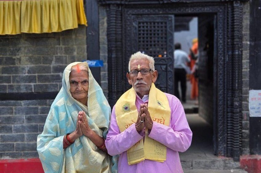 Two individuals in prayer poses at a temple entrance. 1
