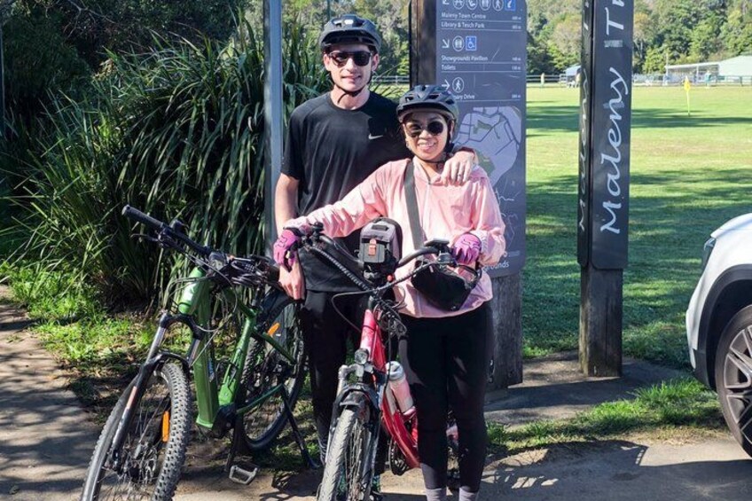 Two people standing next to bicycles, a signpost, and a parked car. 1
