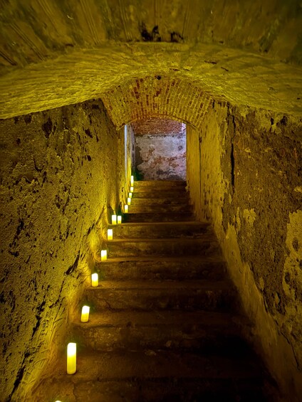 Un escalier en pierre, bordé de bougies, dans un tunnel. 2