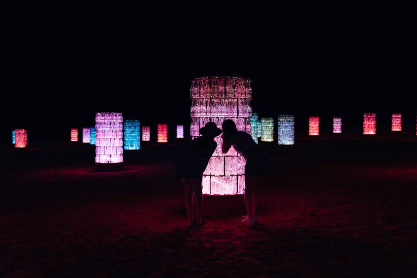 Ein Paar steht vor beleuchteten Bauwerken am Strand bei Nacht. 1