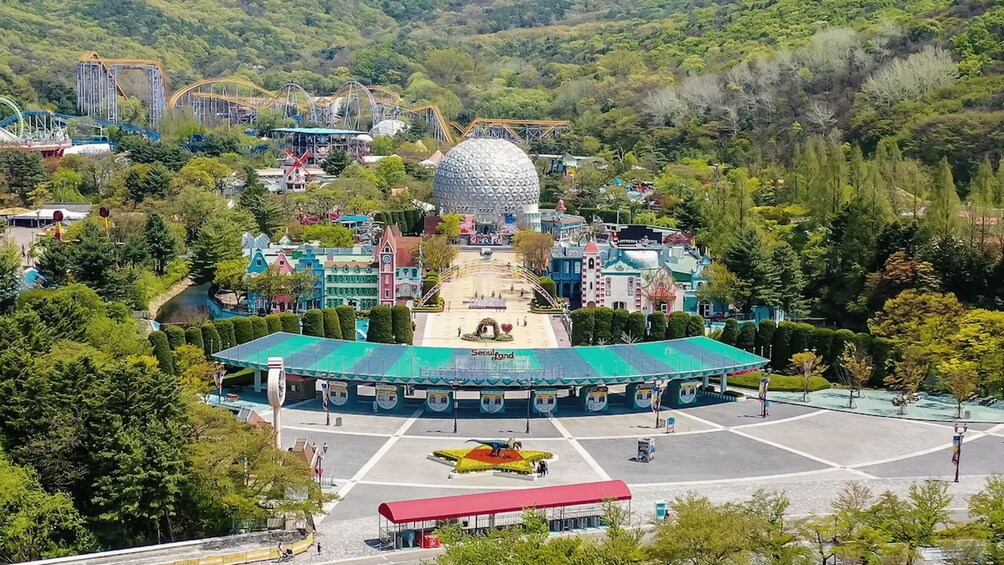 A theme park with a large spherical building, a covered parking area, and surrounding greenery. 1