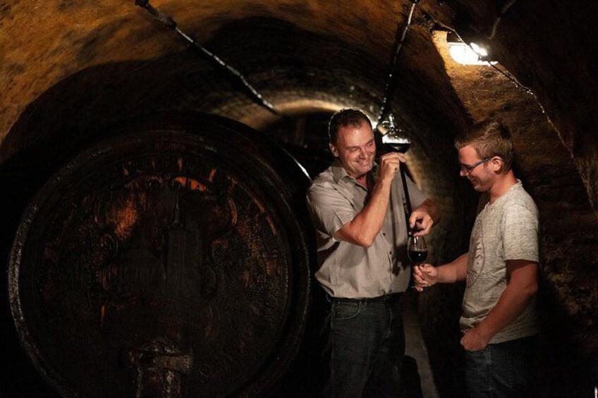 Two people in a dimly lit underground setting, one holding a wine bottle. 3