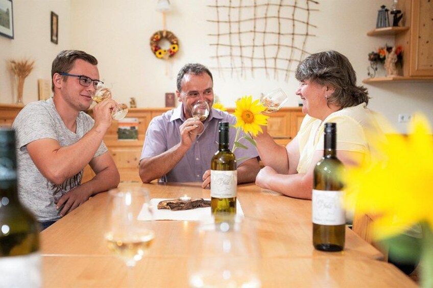 Three people sitting at a wooden table with wine bottles and glasses. 2