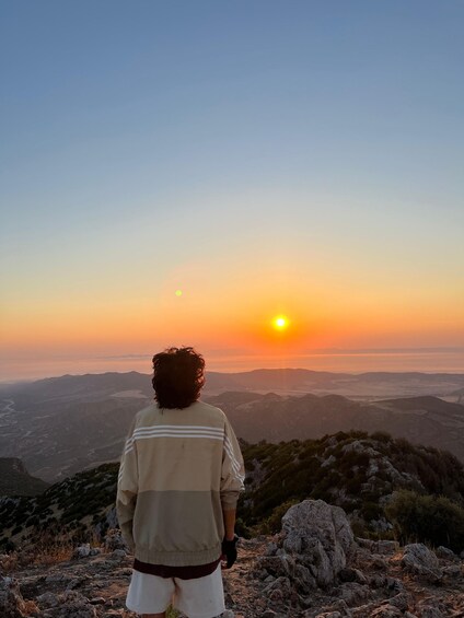Une personne se tient sur un promontoire rocheux, surplombant une vallée, au coucher du soleil. 4