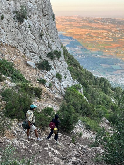 Deux randonneurs sur un sentier de montagne rocailleux, avec vue sur une vallée en contrebas. 2
