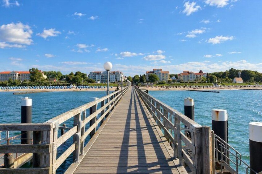A wooden pier extending into a body of water with buildings and greenery in the background. 3