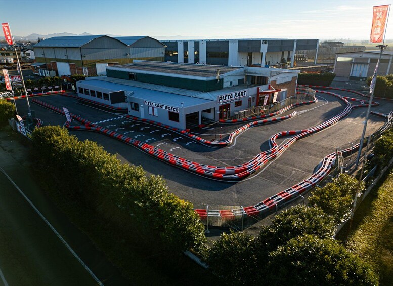 A racing track with a building labeled 'Pista Kart Bosco' and a surrounding area with industrial buildings and flags. 1