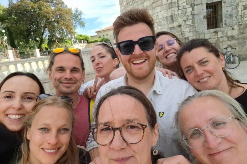 A group of people posing in front of a stone building with a fountain in the background. 1
