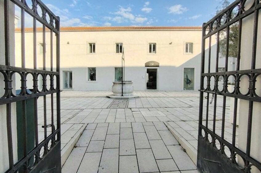 A courtyard with a white building, a fountain, and black metal gates. 2