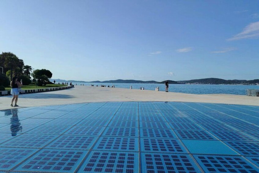 A tiled walkway leading to a beach with people walking and standing. 5